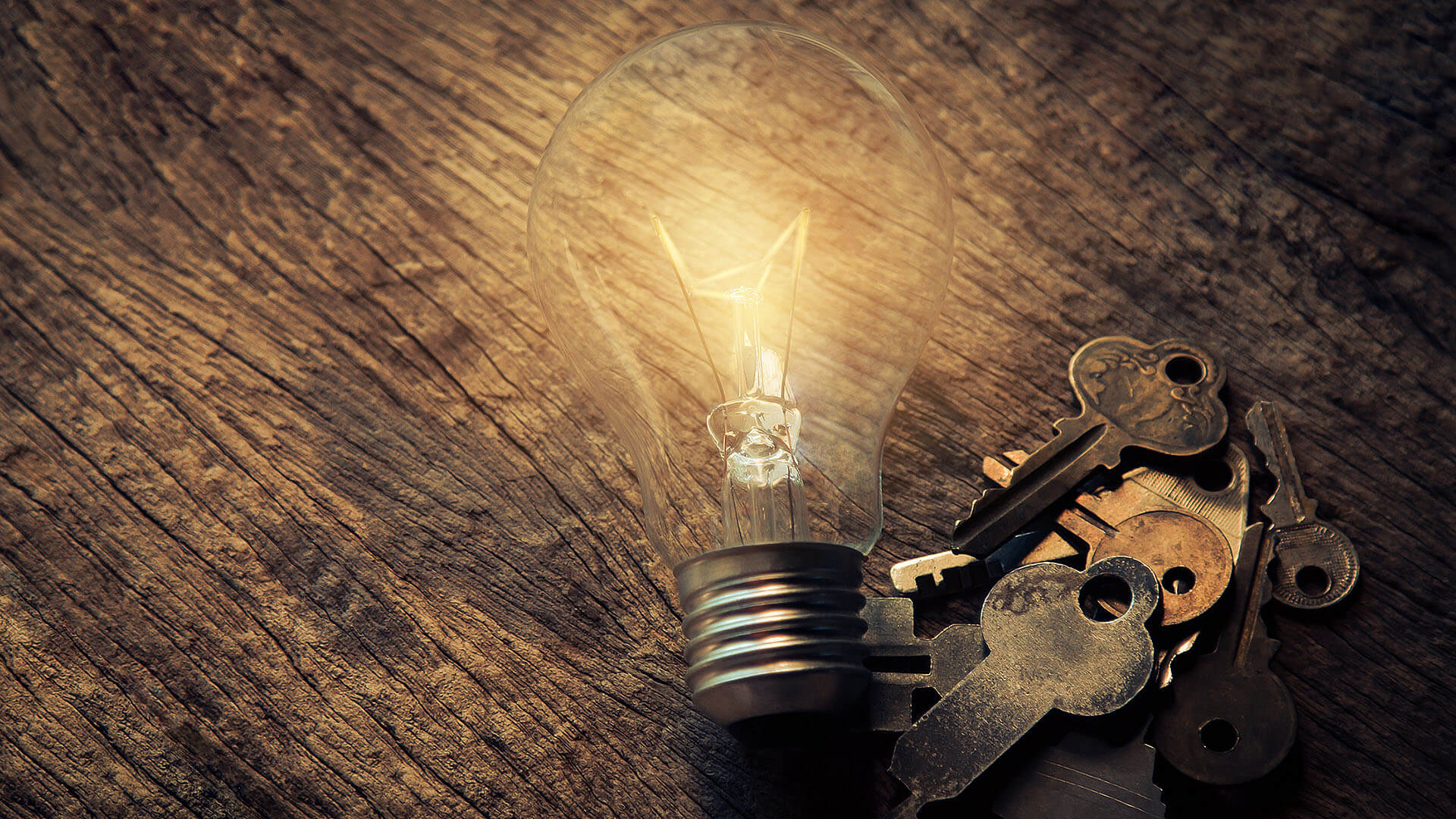A lit light bulb beside a heap of old keys