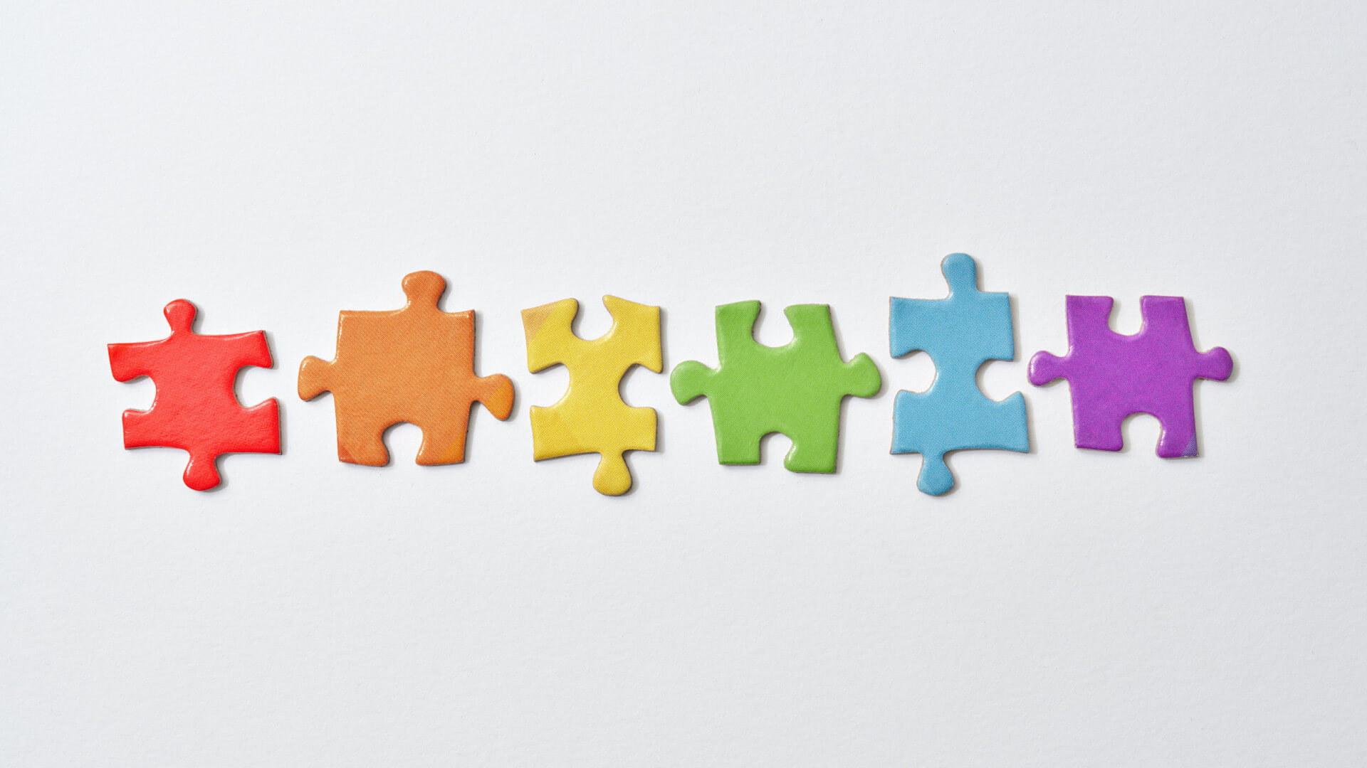 Six puzzle pieces in the colors of the rainbow, side by side on a white surface