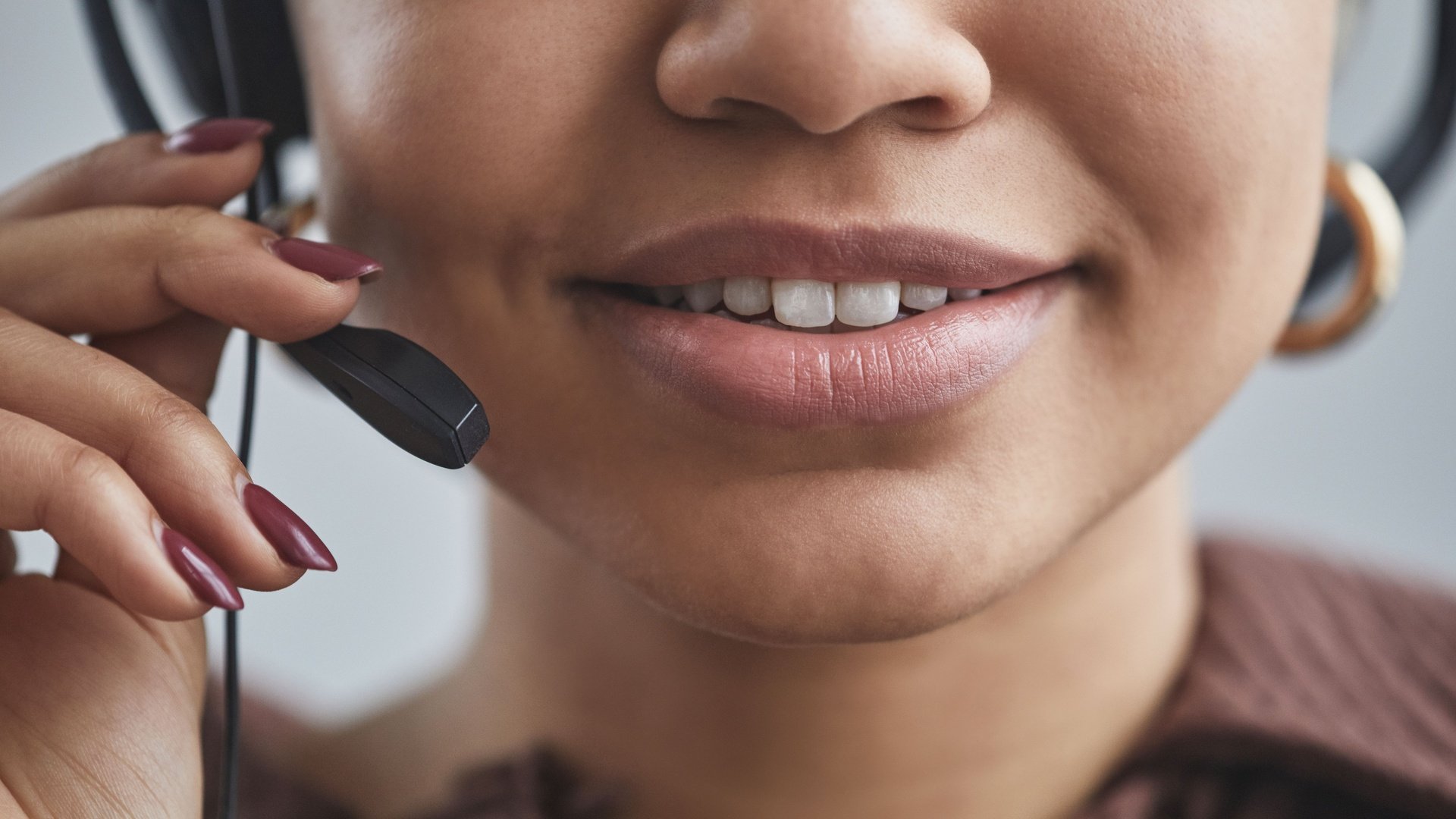Primo piano di una donna sorridente che parla nel microfono della sua cuffia, una mano sull'asta
