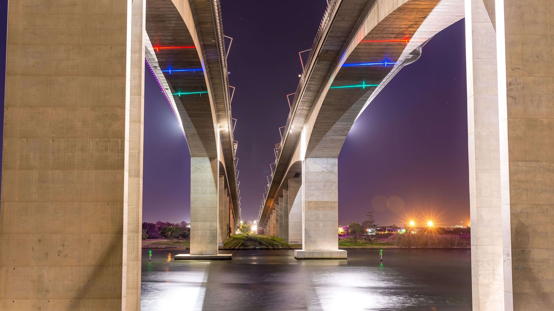 Two bridges side by side over a river at night